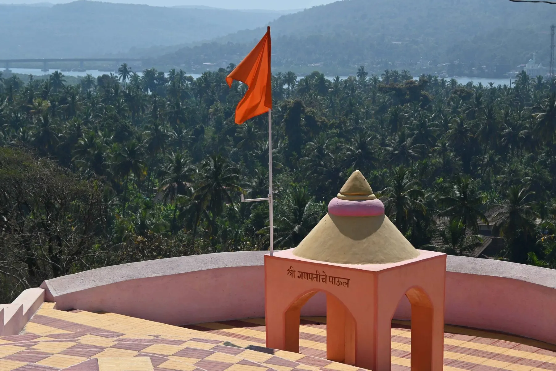 Saffron flag and small shrine on the Anjarle cliff above coconut groves