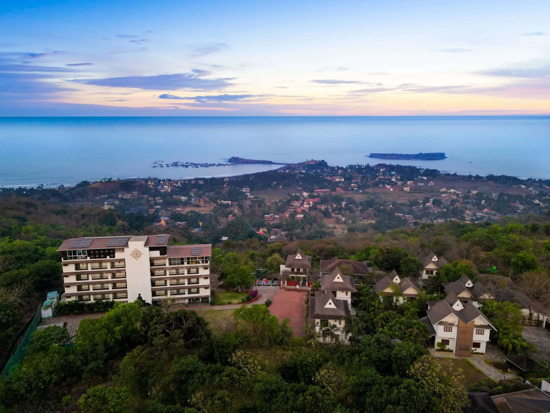 Aerial view of a Dapoli resort among green hills with the sea on the horizon